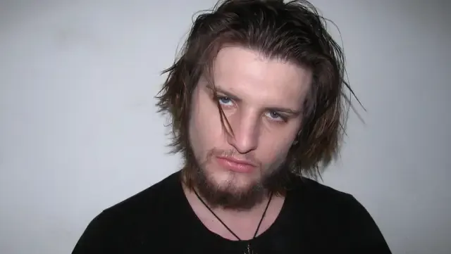 Alternative man, with red lips, piercing grey eyes, and full brown hai
